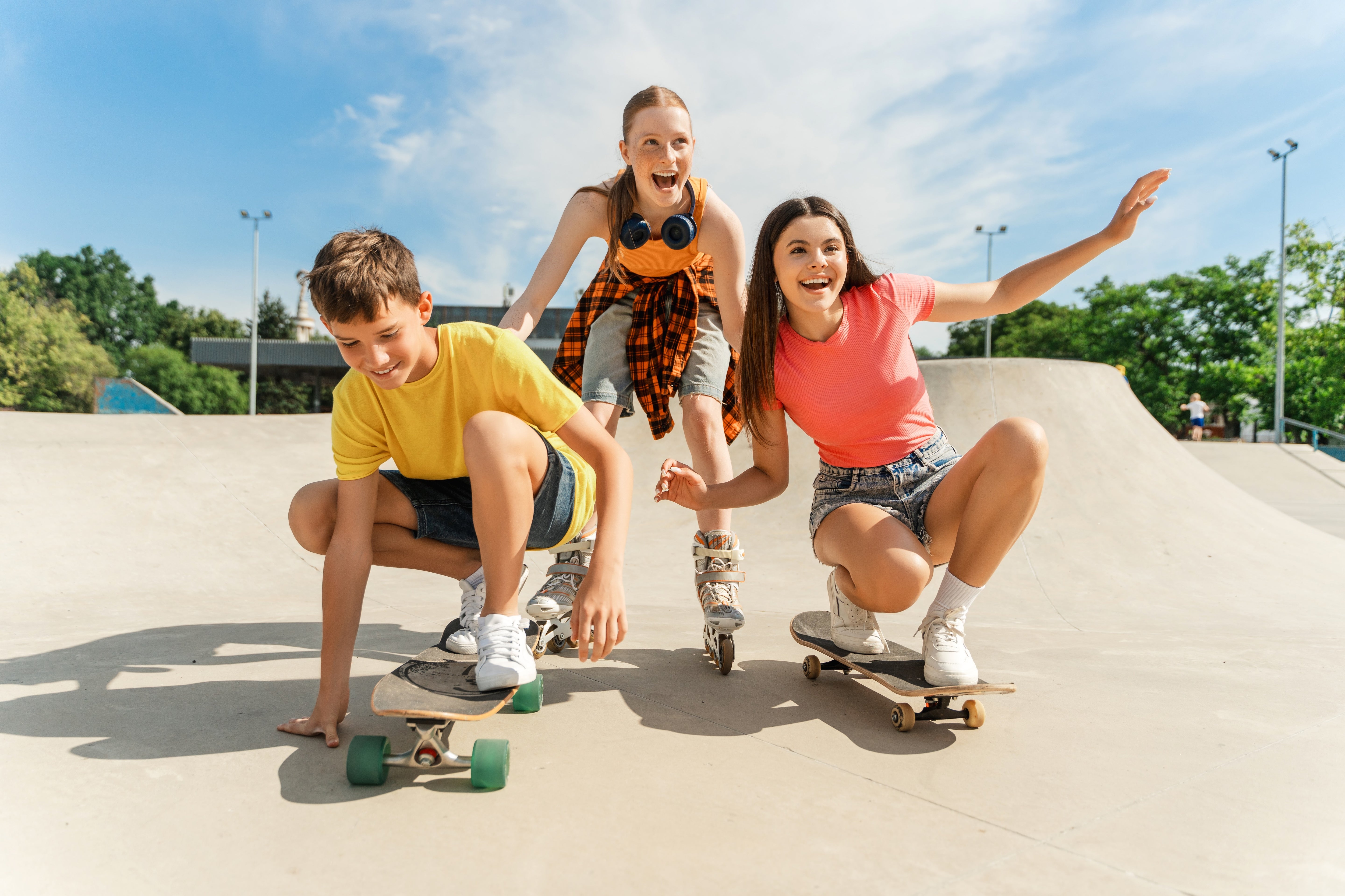 Three young people skateboarding at a park on a sunny day.