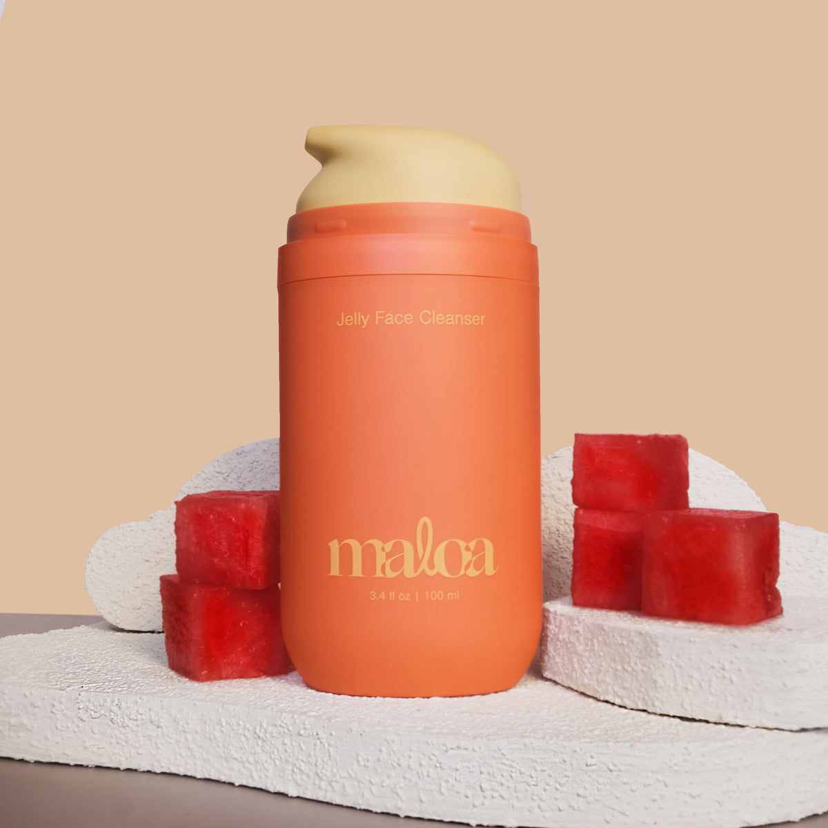 An terracotta bottle of MALOA Jelly Face Cleanser with the top off, exposing the yellow pump, stands centered on a textured white stone slab, flanked by watermelon cubes against a warm beige background 