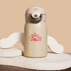 A cream-colored insulated water bottle with a red sun and wave logo, displayed on a textured beige stone prop against a solid beige background.