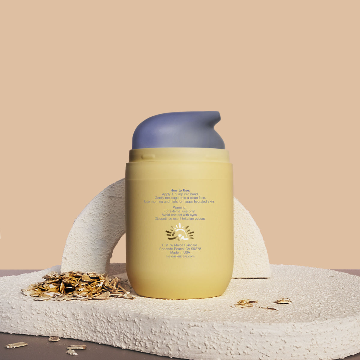 The back of a pale yellow Triple Cloud Face Moisturizer with the brand name 'MALOA' printed in blue on the front, styled on a textured stone surface with scattered oats against a warm beige background. Back exposing the metalic gold foil logo